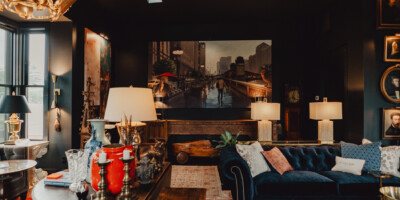 Eclectic living room with dark walls, a blue sofa, various lamps, art, and vintage decor accents.