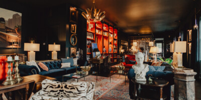 Eclectic lounge with velvet sofas, patterned chairs, bookshelves, art, warm lighting, and a white bust on a central table.